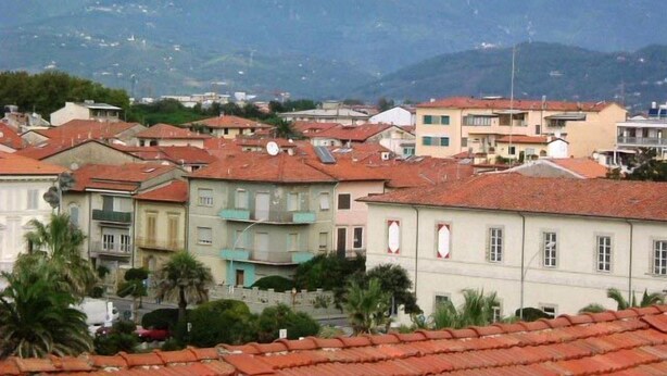 A residential area with buildings featuring red-tiled roofs, surrounded by mountains. - Hotel Bella Riviera (Viareggio)