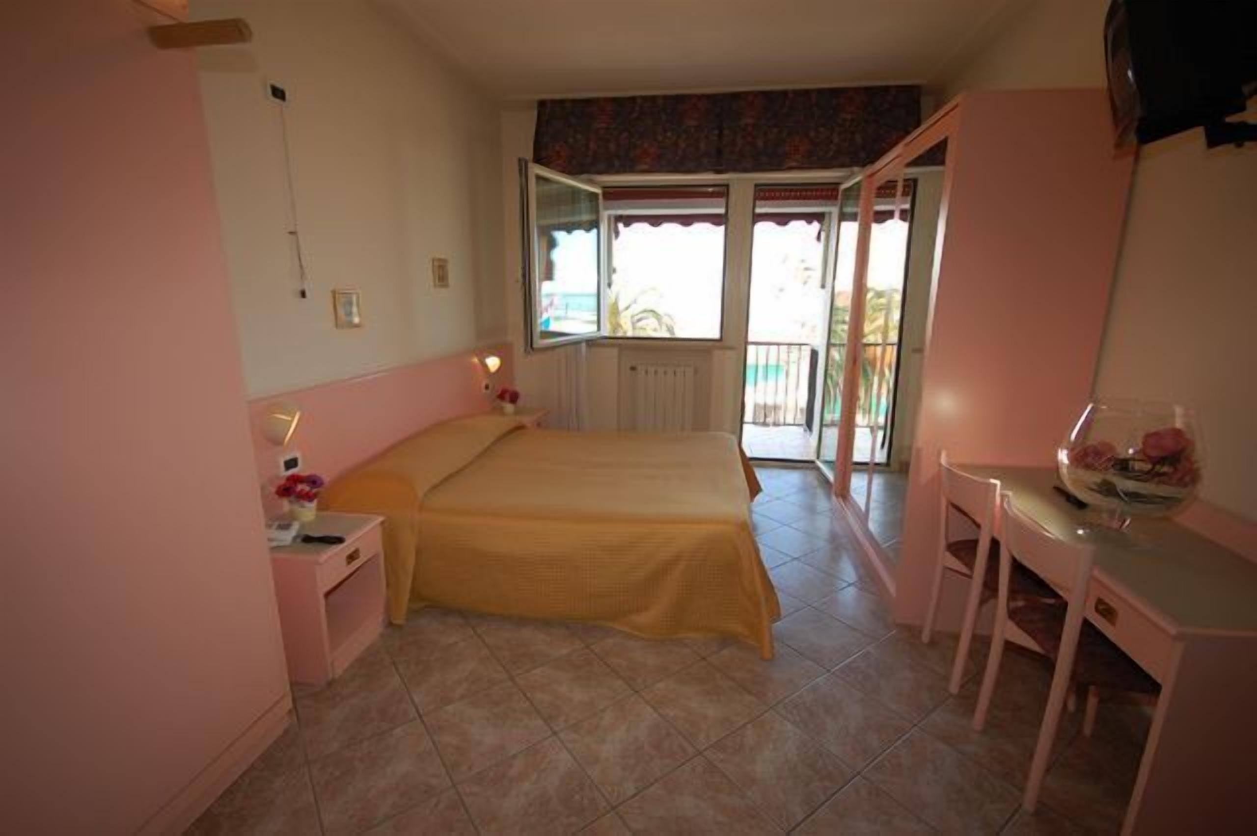 Ein Schlafzimmer mit einem Bett, einem Schreibtisch und einem Stuhl. Ein Fenster bietet einen Ausblick nach draußen.