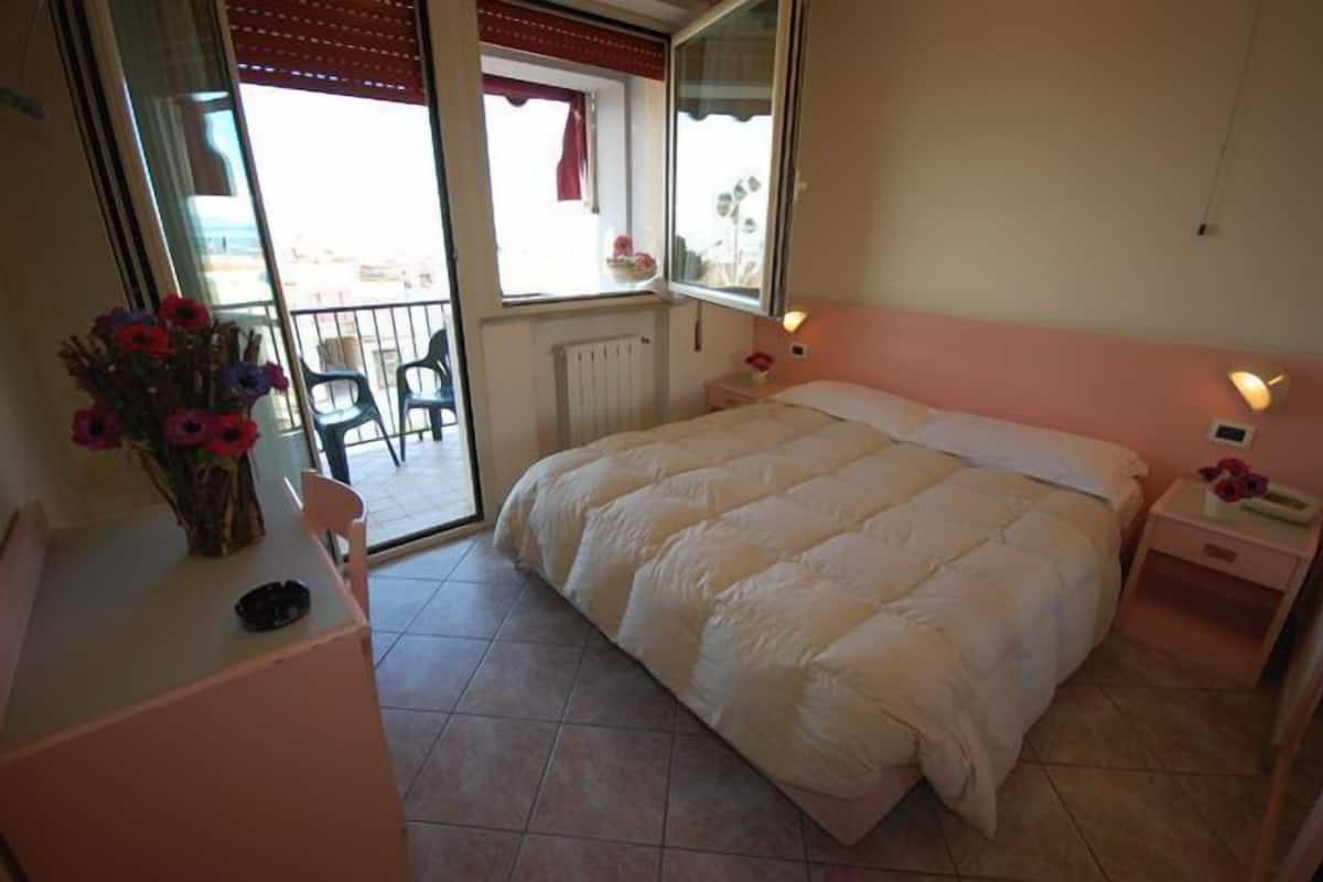 A bedroom with a bed, a dresser, a chair, a window, and a balcony.