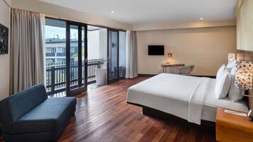 A hotel room with a large bed, a sofa, a desk, and a balcony with a view of buildings.
