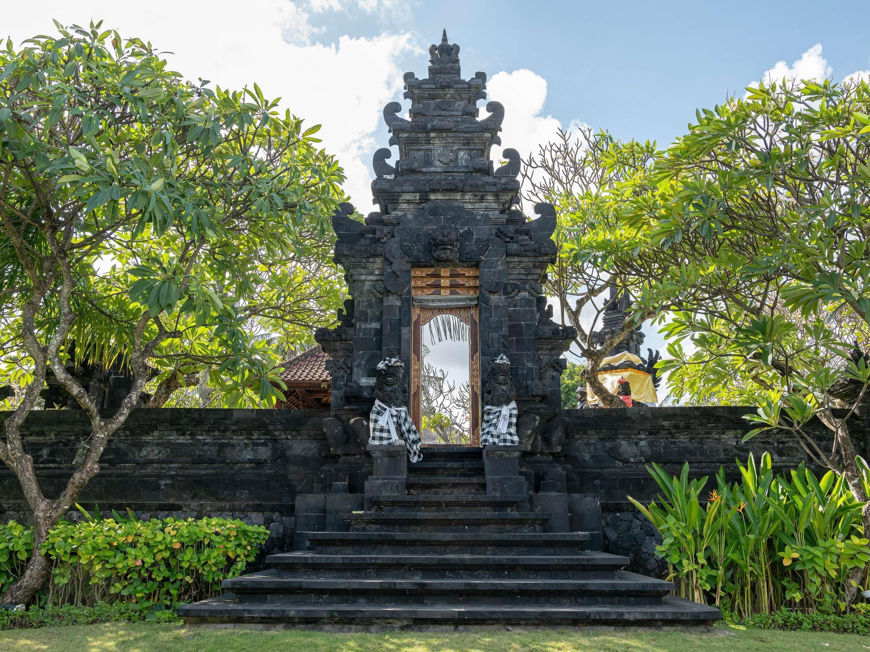 Un templo balinés tradicional con un acceso central, flanqueado por escalones de piedra y abundante vegetación.