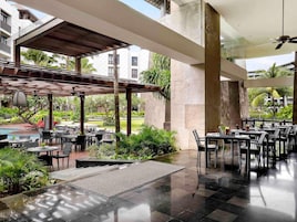 Un espacio de comedor al aire libre con mesas y sillas, rodeado de vegetación y una piscina.