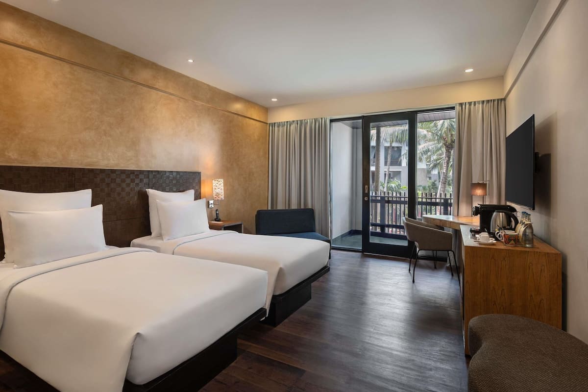 A hotel room with two beds, a desk, a chair, a TV, and a balcony with curtains.