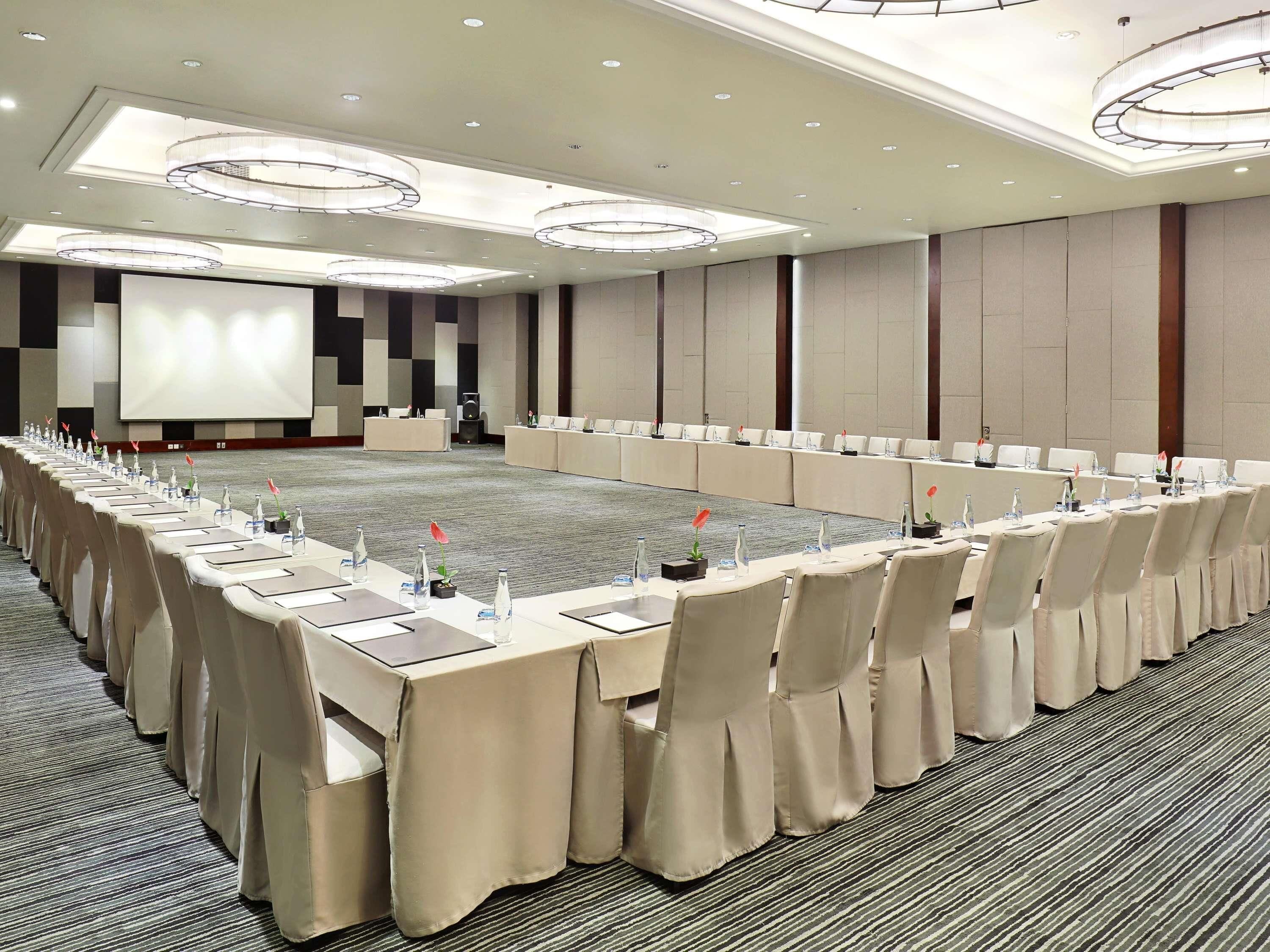 A conference room with long tables, chairs, and a large screen.
