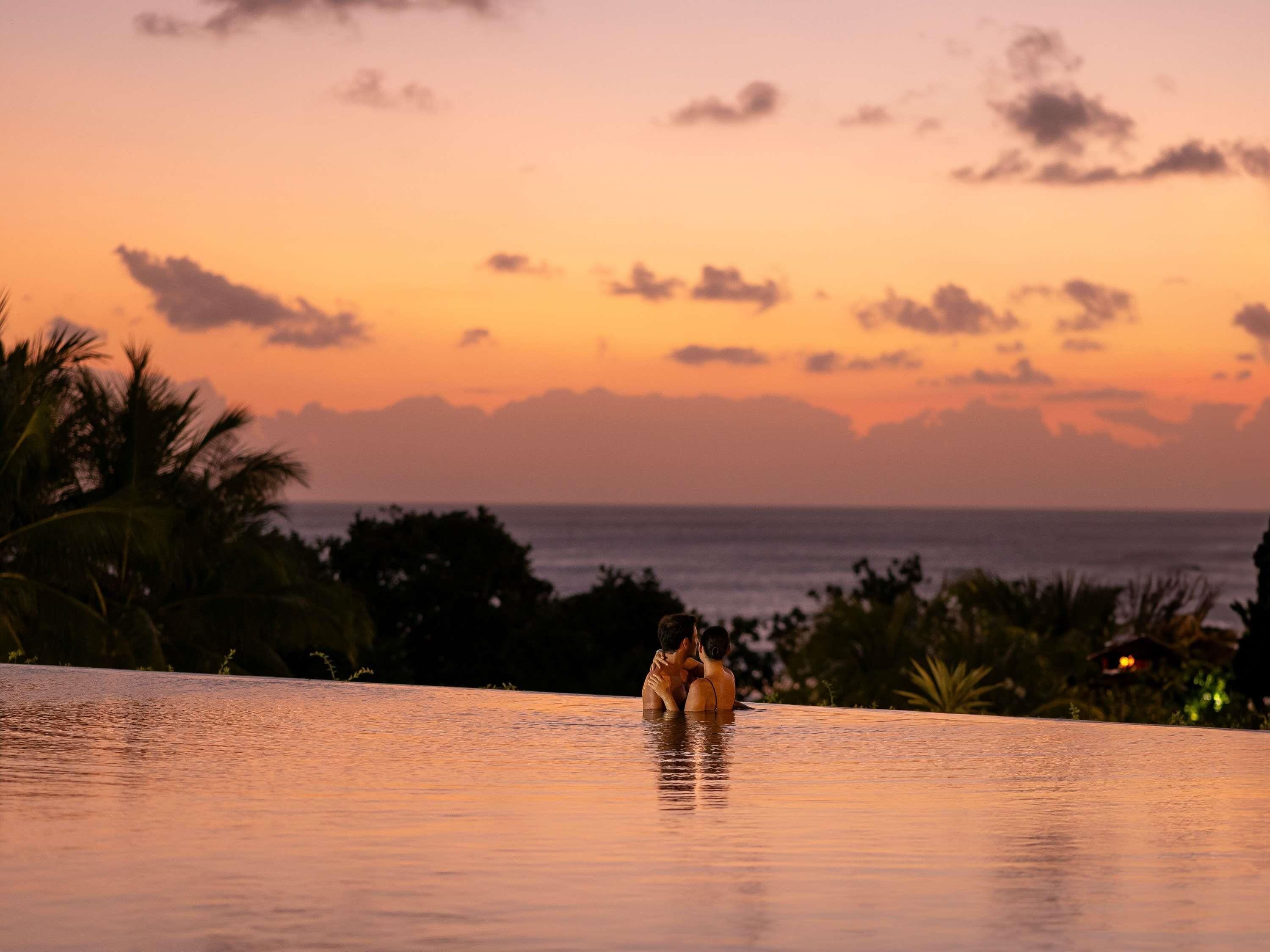 A couple in a swimming pool with a sunset view.