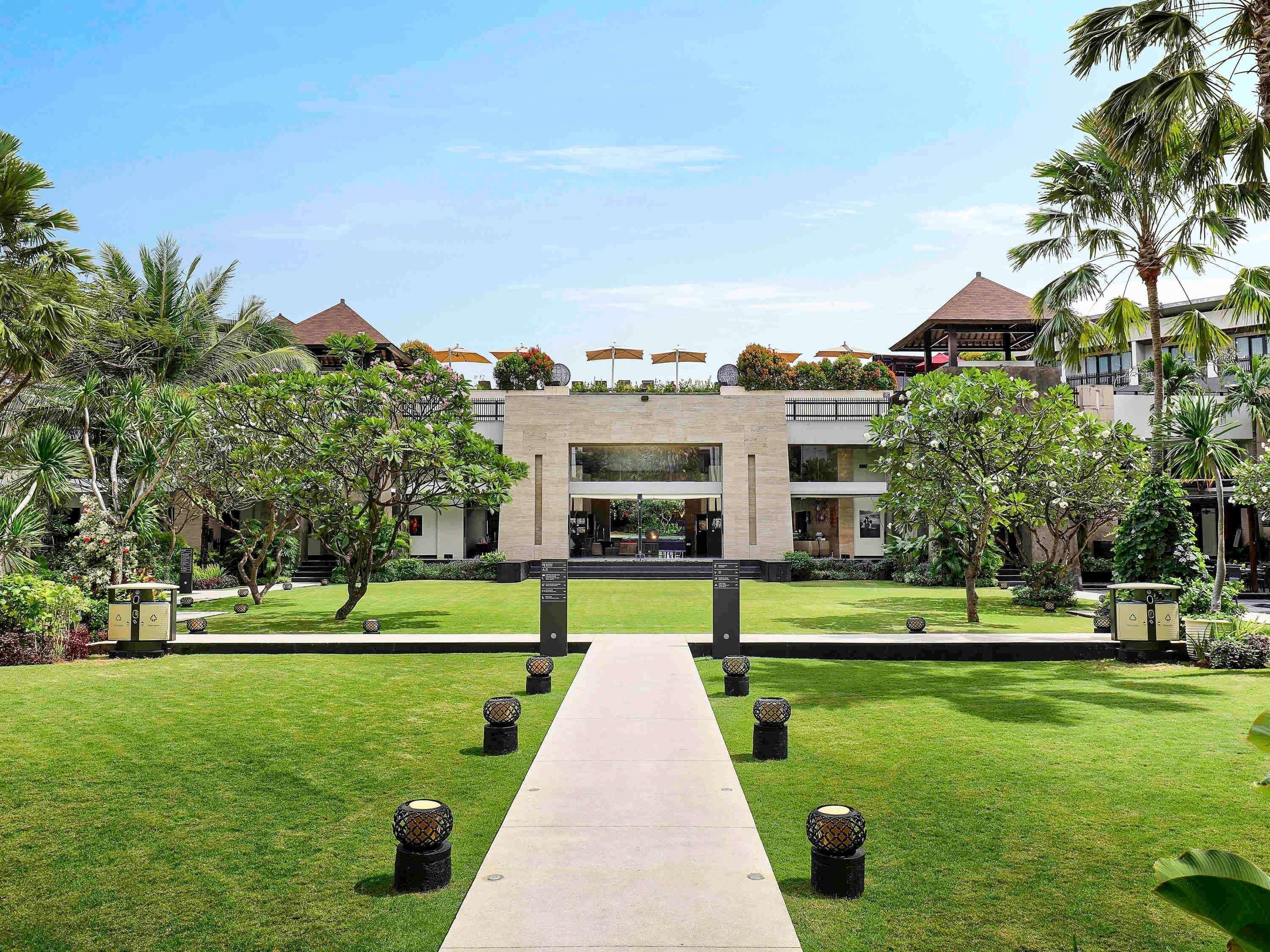 A modern hotel with a central entrance, surrounded by well-maintained lawns and palm trees.