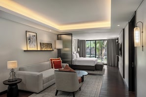 Une chambre d’hôtel moderne, équipée d’un canapé, d’un fauteuil, d’une table de chevet, d’une lampe et d’un lit donnant sur l’extérieur.