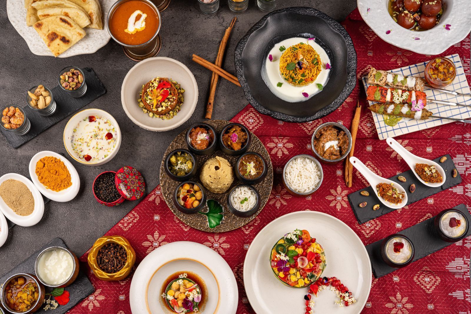 Diversos pratos e alimentos dispostos sobre uma mesa com toalha de mesa estampada em vermelho.
