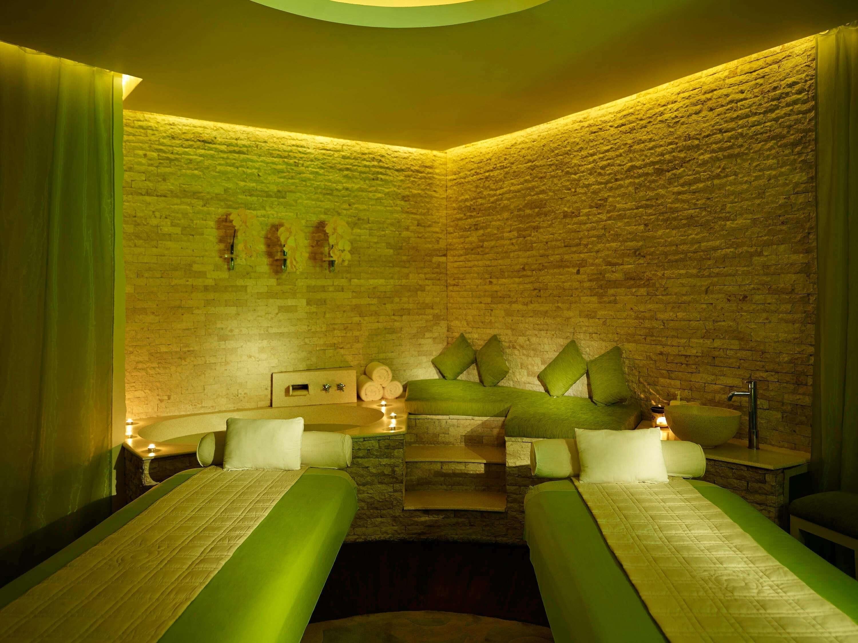 A spa room with two beds, a stone wall, and a small table with candles.
