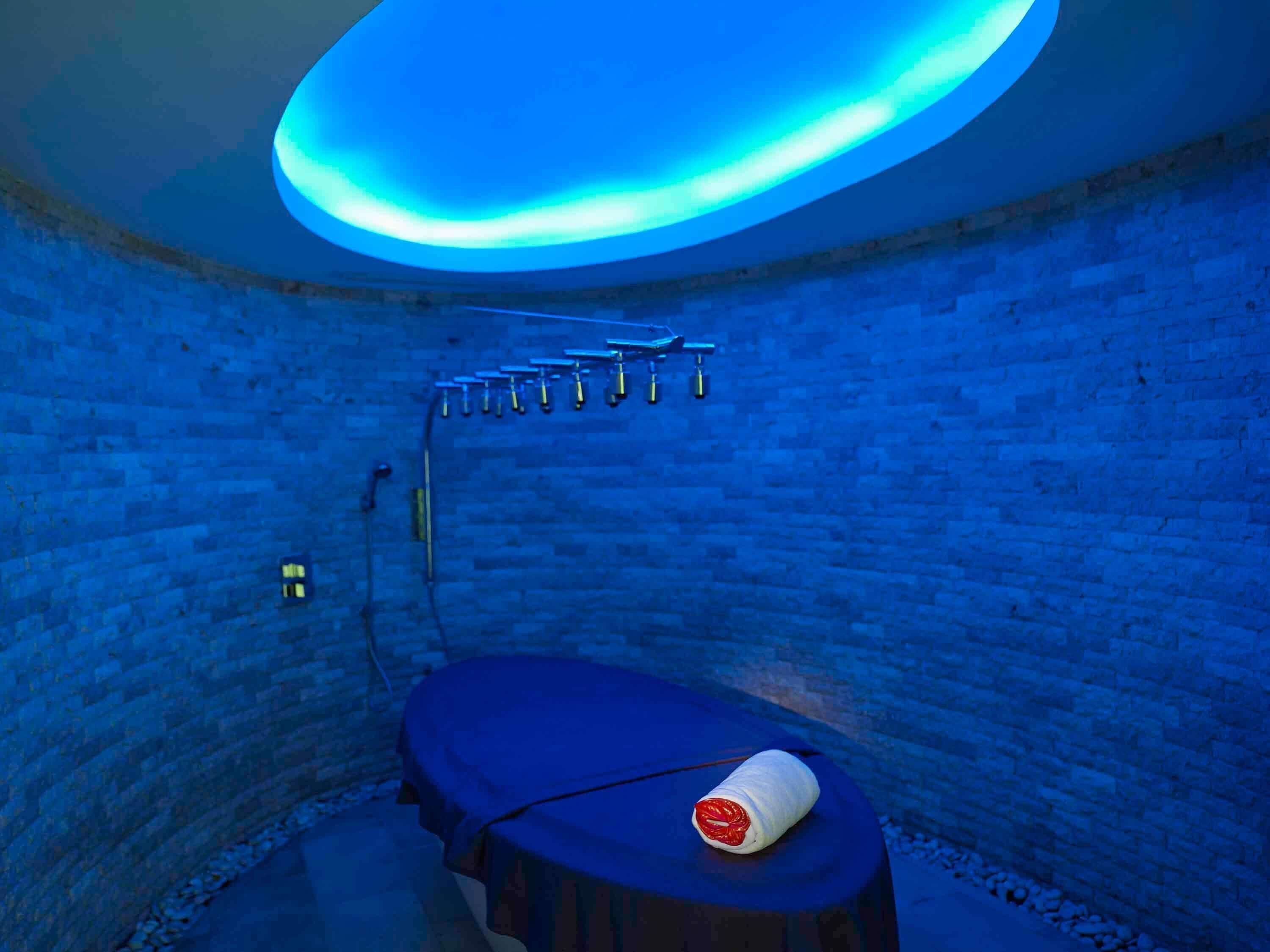 A room with a brick wall, a blue ceiling, and a bed with a white pillow.