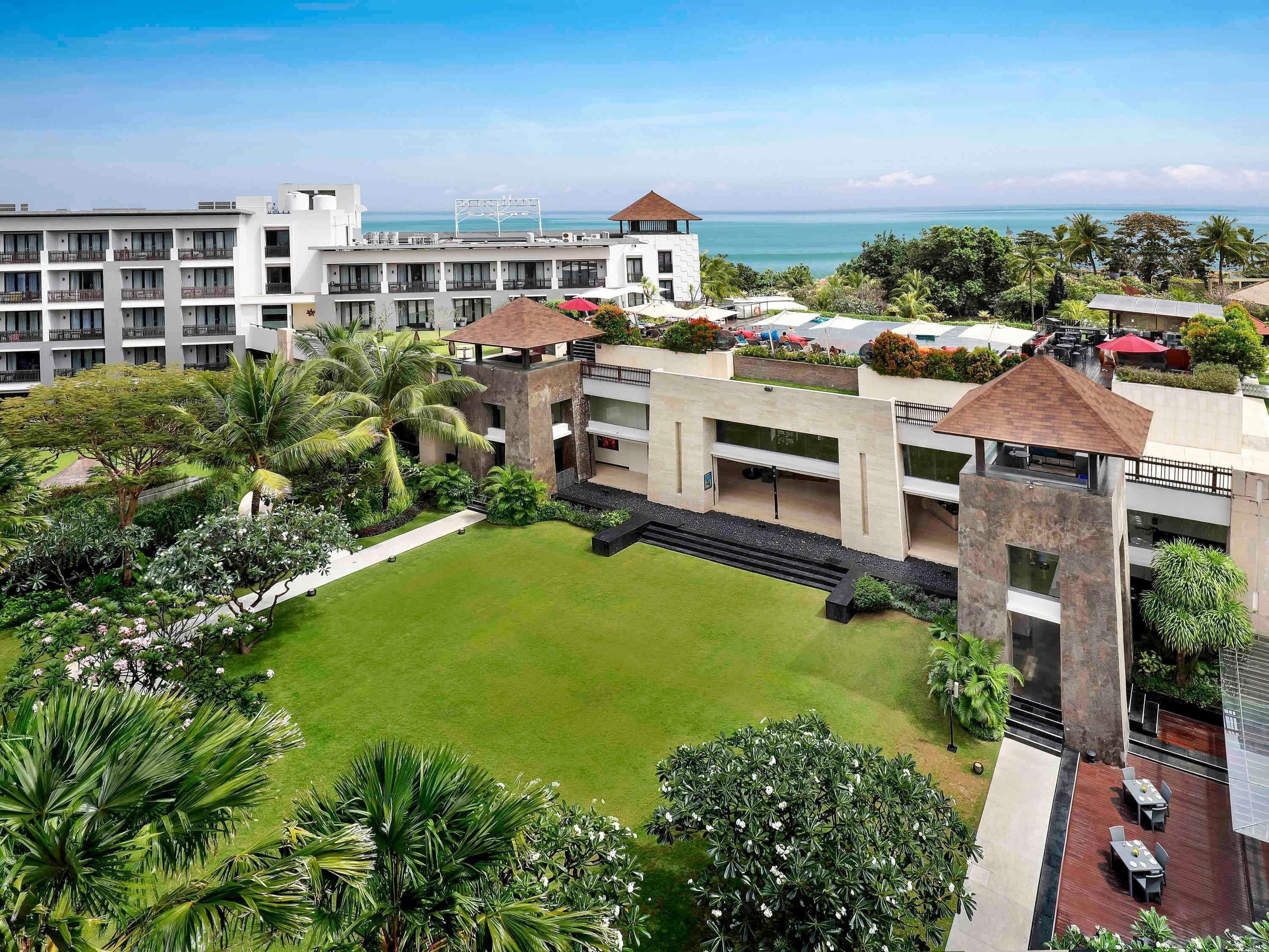 A hotel with multiple buildings, a courtyard with greenery, and a view of the ocean.