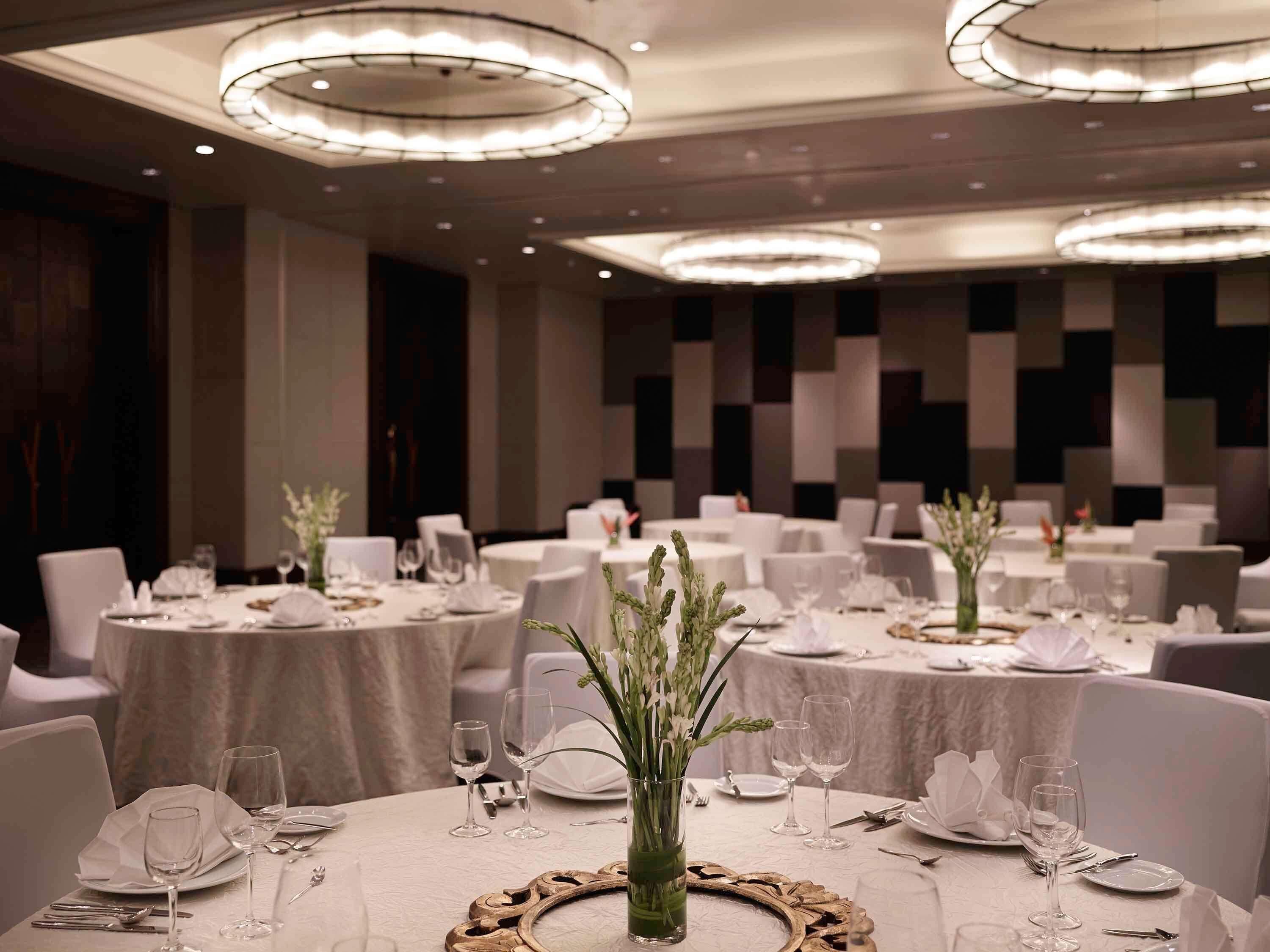A banquet hall with round tables, white tablecloths, and elegant lighting fixtures.