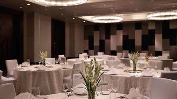 A banquet hall with round tables, white tablecloths, and elegant lighting fixtures.