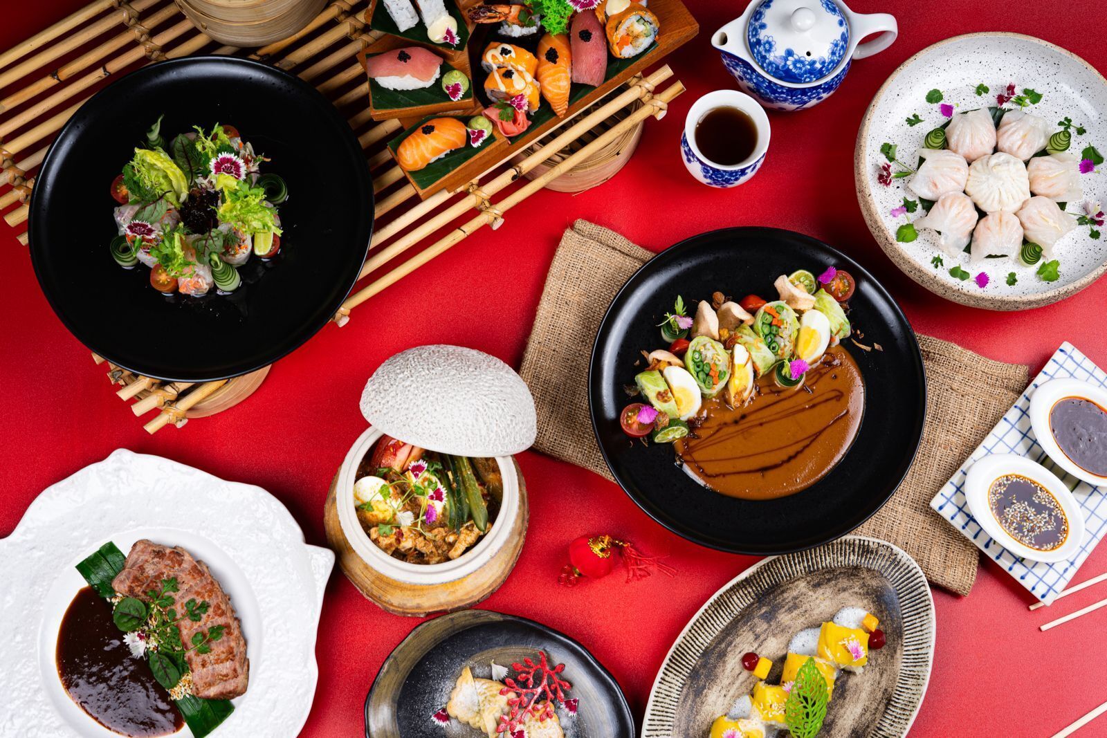 Una variedad de platos, incluyendo sushi, dumplings y un tazón de sopa, sobre una mesa roja.