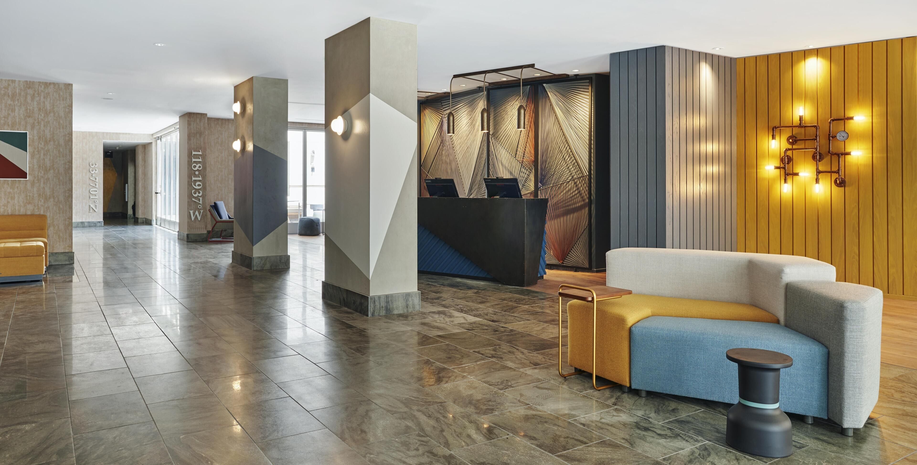 A modern hotel lobby with a reception desk, seating area, and a patterned wall.