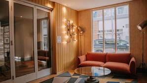 A modern interior with a glass door leading to a room, a round glass table, a red sofa, and a patterned rug.