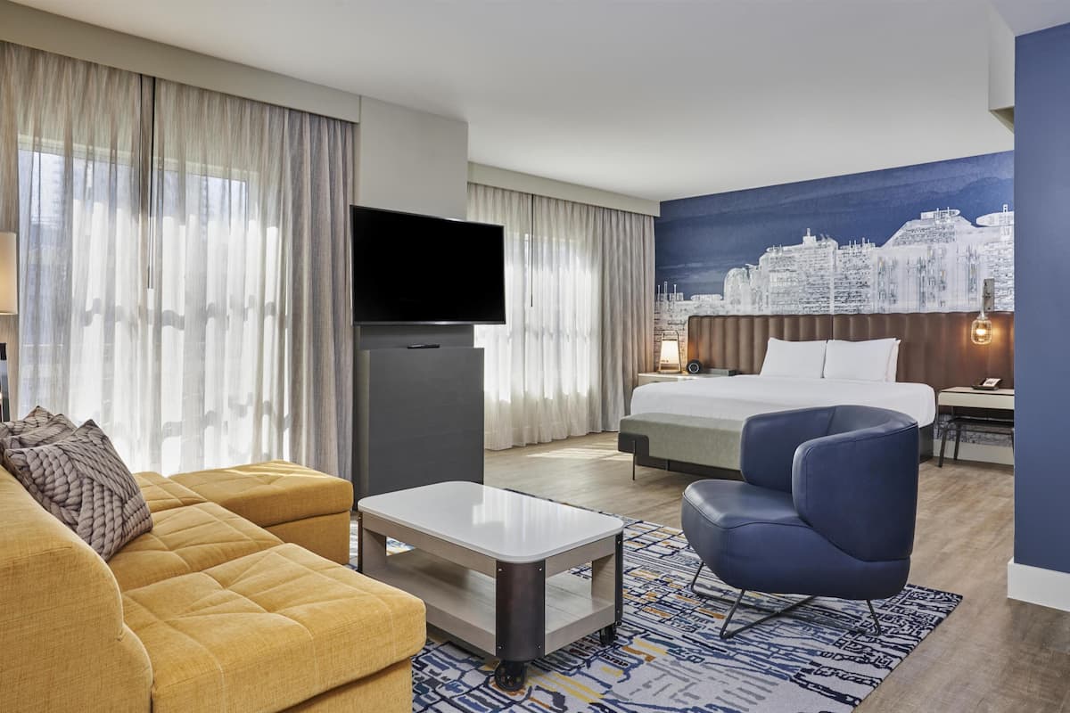 A hotel room with a bed, a sofa, a TV, and a cityscape mural.
