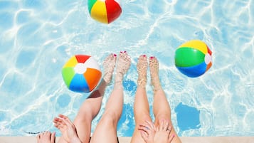 Una piscina con agua azul cristalina y tres pelotas de playa flotando.