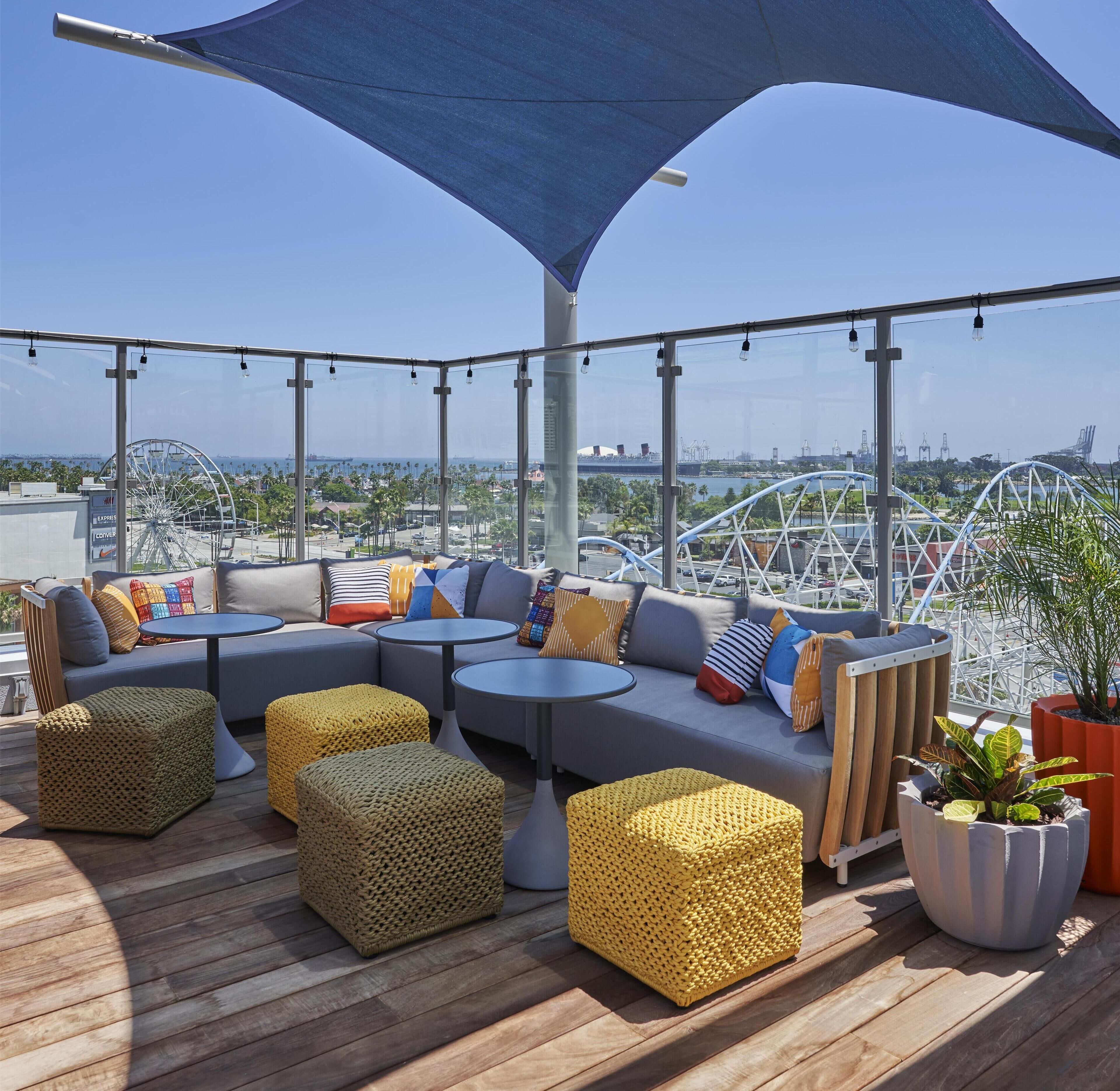 Una terraza en la azotea con zona de estar, vista a una noria y un paraguas grande que da sombra.