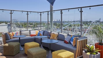 Una terraza en la azotea con zona de estar, vista a una noria y un paraguas grande que da sombra.
