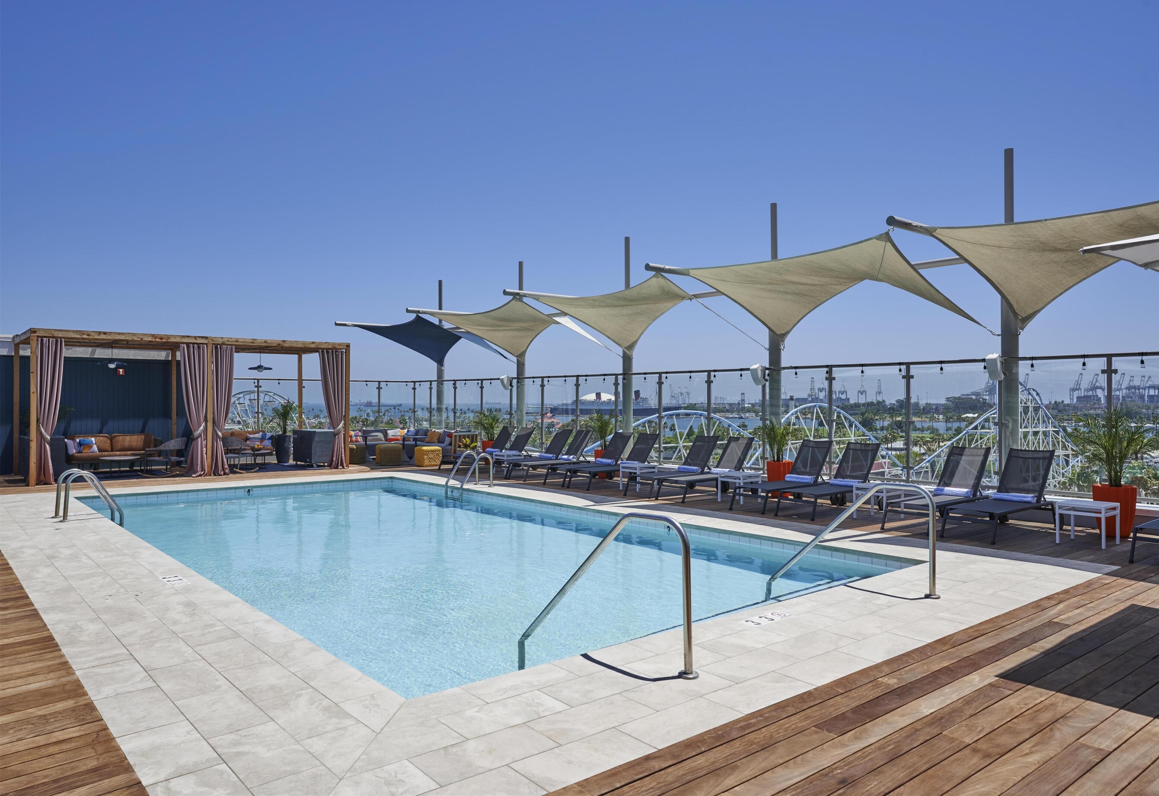 A rooftop pool with lounge chairs and umbrellas, surrounded by a wooden deck.