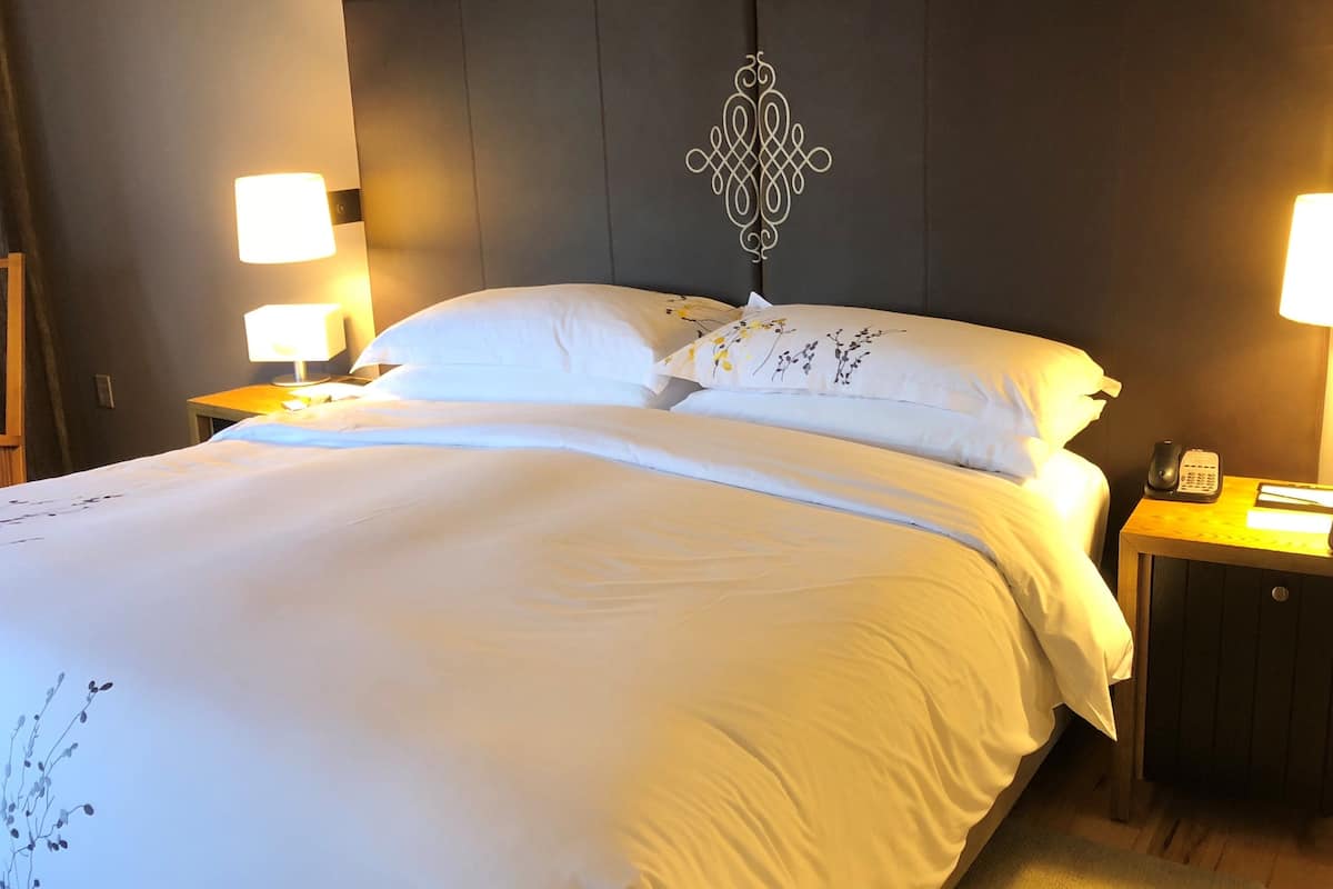 A neatly made bed with white linens and floral pillows, a dark headboard with a decorative pattern, and bedside lamps on wooden nightstands.