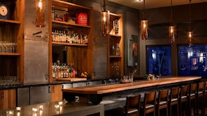 A bar area with a long counter, wooden shelves with bottles, and hanging pendant lights.