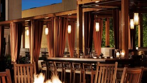 An outdoor seating area with a fire pit, wooden chairs, and a bar with a stone countertop.