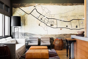 A modern living room with a large map mural, a sofa, two armchairs, a coffee table, and a bar area.
