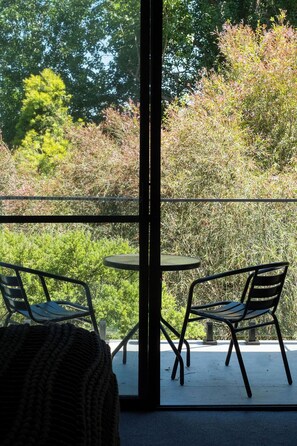 A balcony with two tables and chairs, overlooking a garden with various plants and trees.