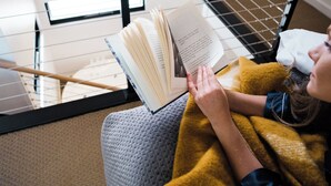 A person reading a book in a room with a window, a wooden railing, and a hanging light fixture. - Chimes Spa Retreat (Shadforth)