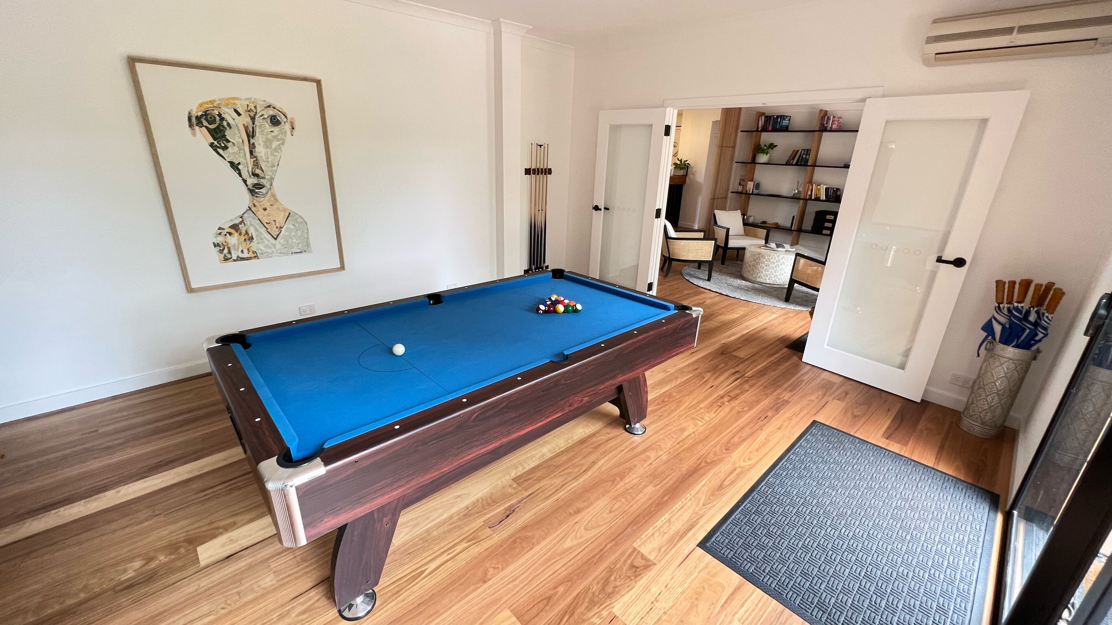 A pool table with a blue felt surface, wooden flooring, and a framed artwork on the wall.