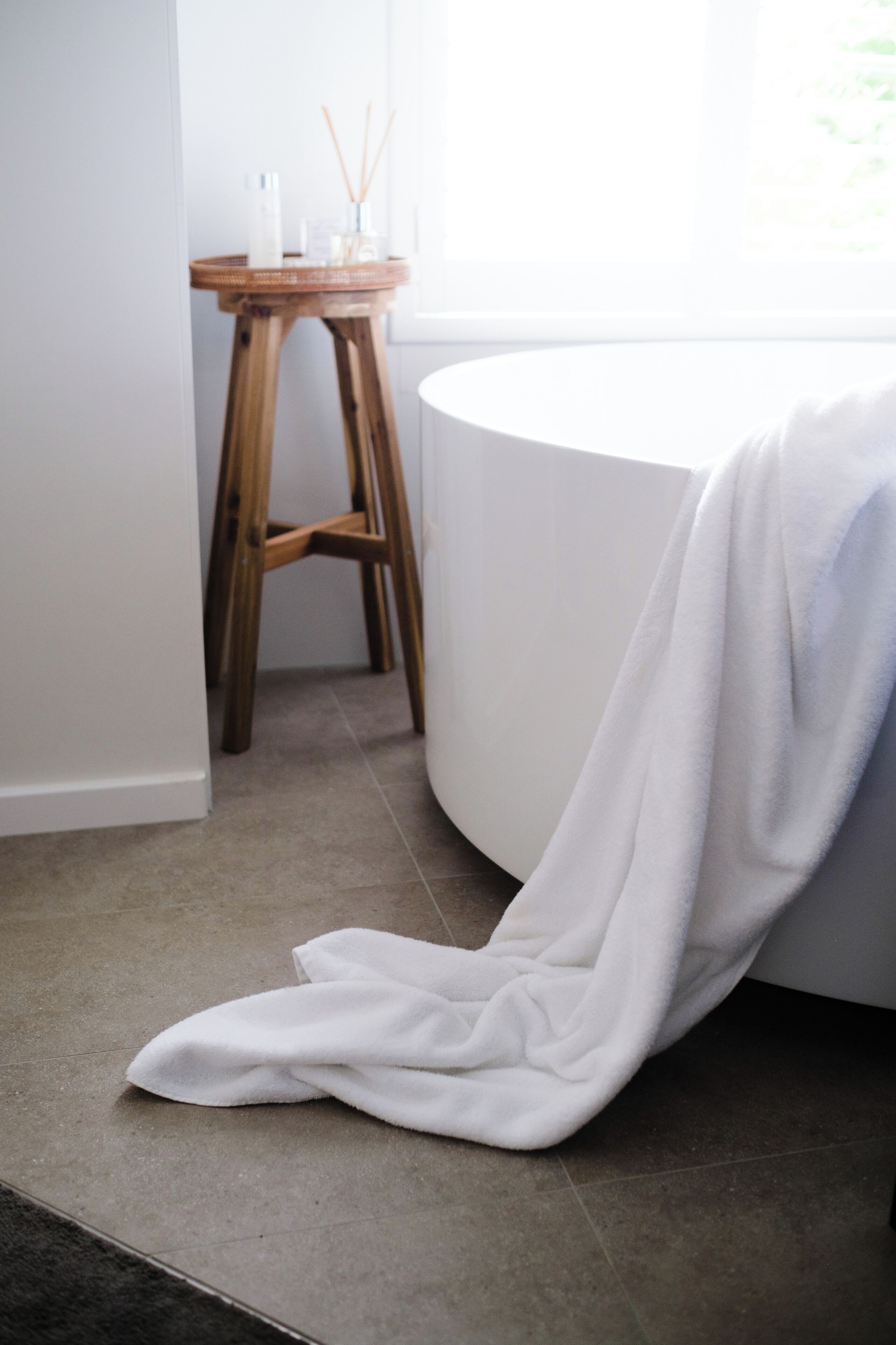 A bathroom with a white bathtub, a wooden stool, and a white towel on the floor.