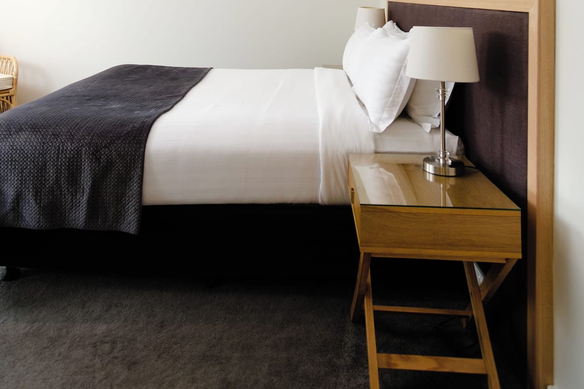 A neatly arranged hotel room with a bed, bedside table, lamp, and a chair.