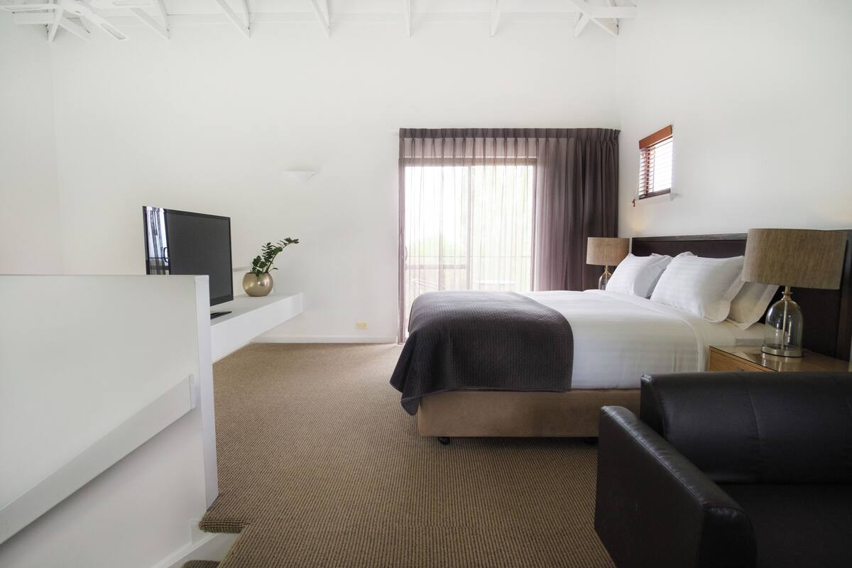 A hotel room with a bed, a desk with a computer, a chair, and a lamp.