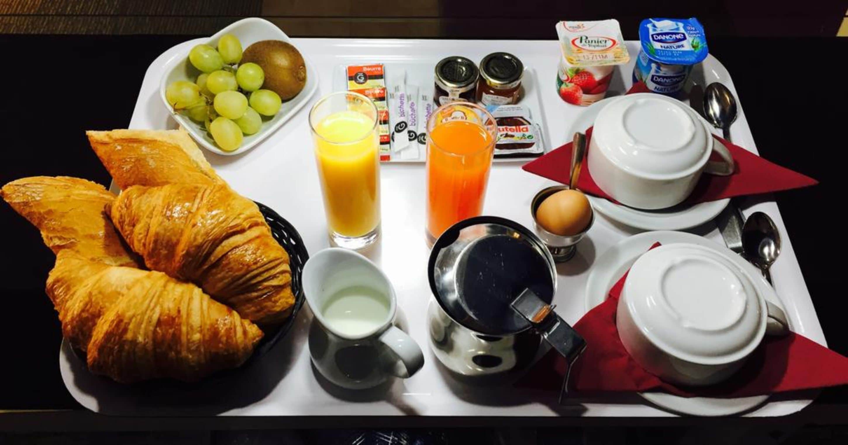 Bandeja de desayuno con cruasanes, uvas, jugo de naranja, café y aderezos.