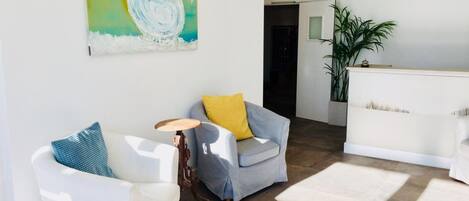 Un salon moderne avec un canapé blanc, un fauteuil gris et une petite table en bois. Un tableau est accroché au mur, et une plante se trouve dans un coin.