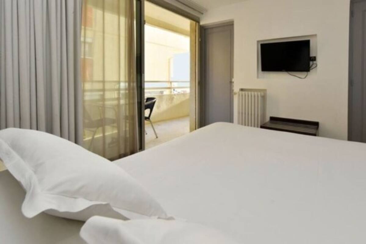 A hotel room with a bed, a TV mounted on the wall, and a view of the outside balcony.