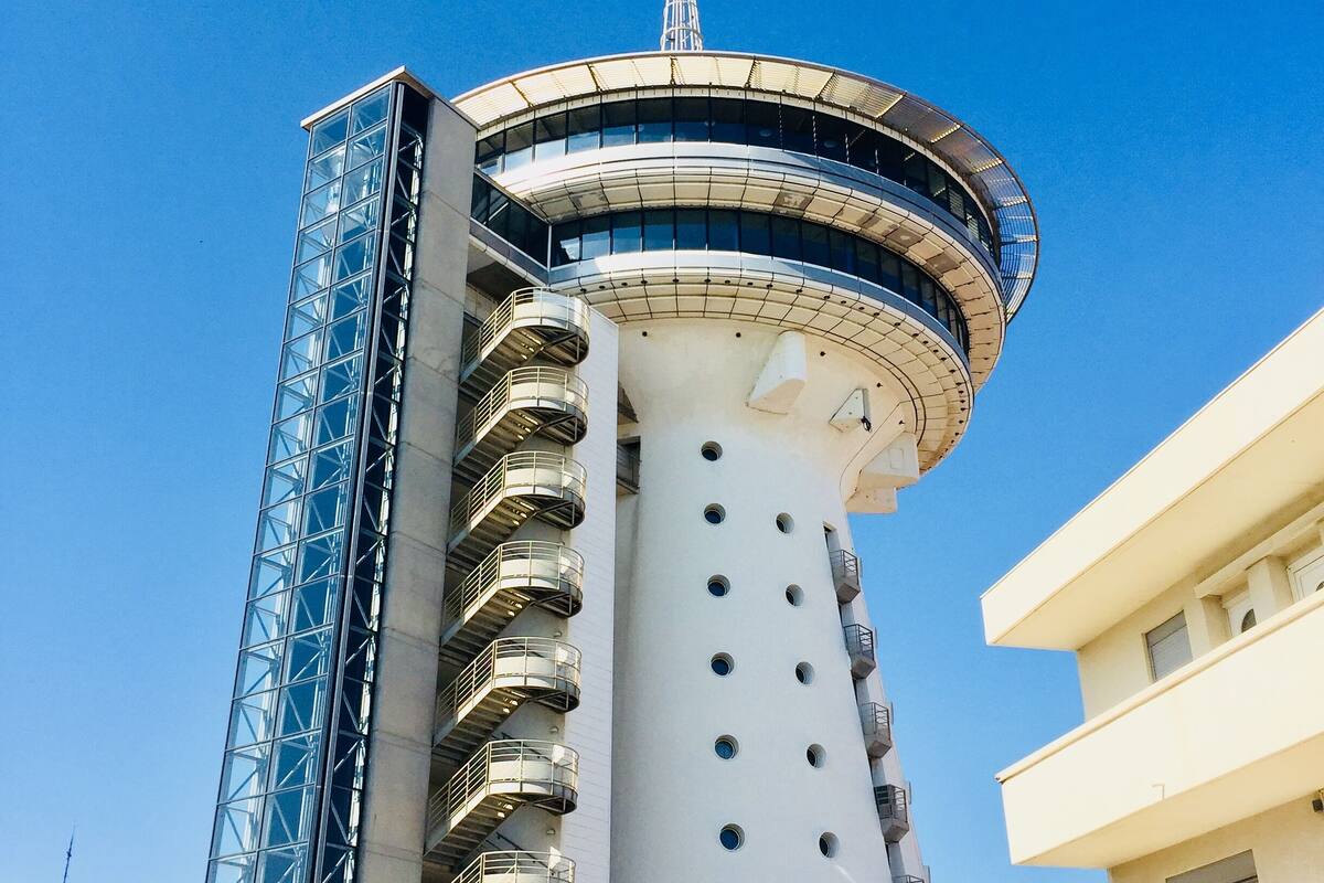A modern building with a cylindrical tower, multiple balconies, and a spire on top.