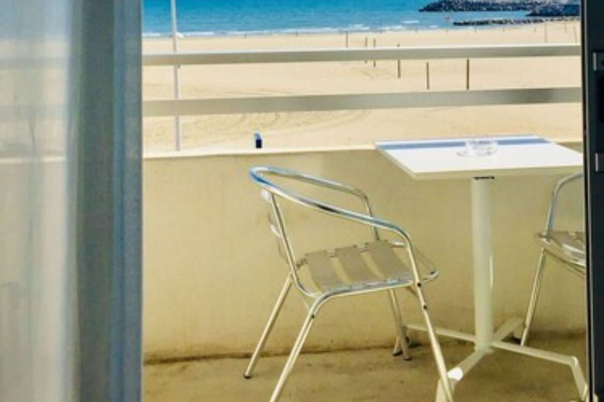 A balcony with a view of the beach, a table, and two chairs.