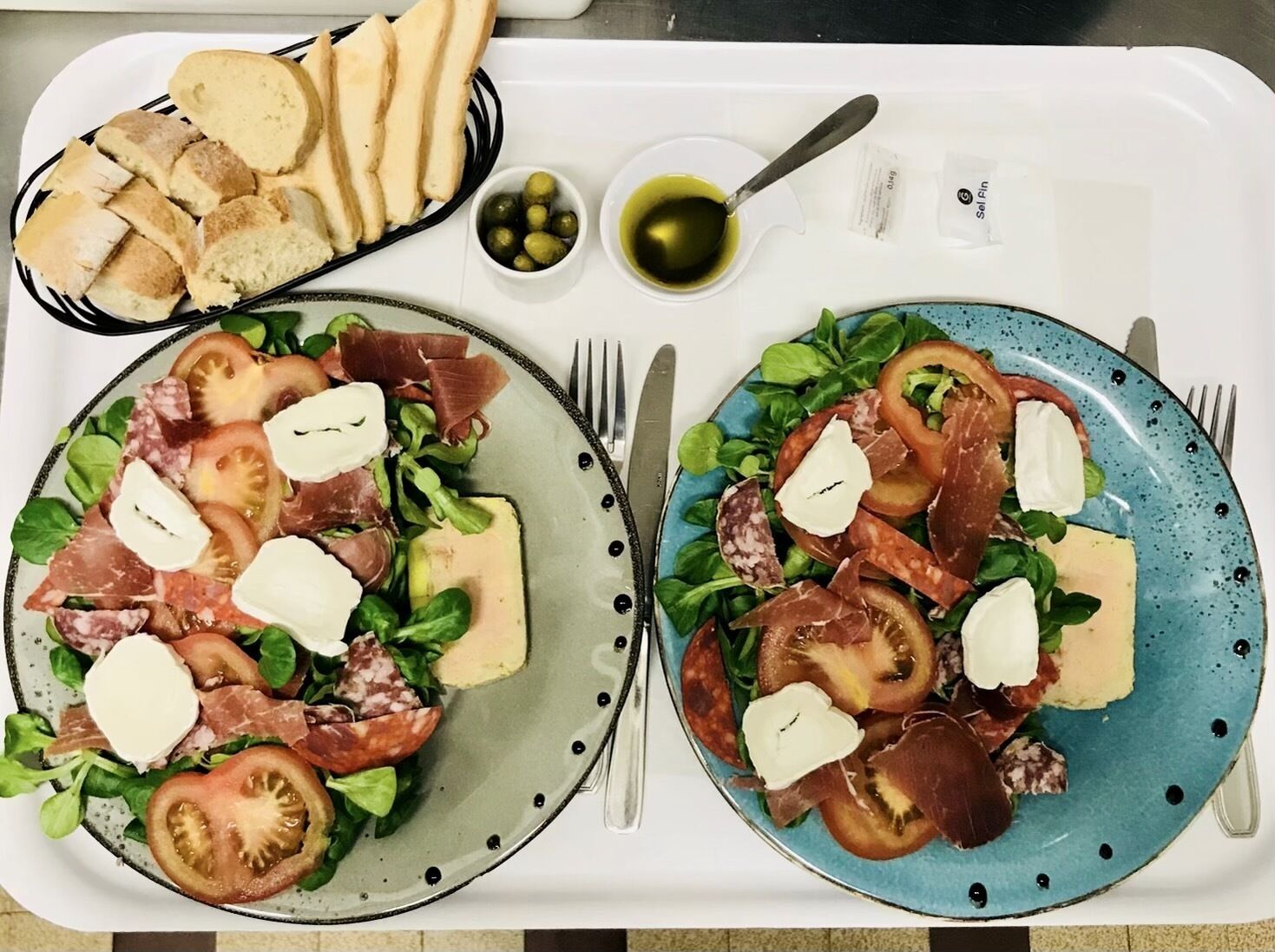 Two plates of food with bread and olives on a tray.