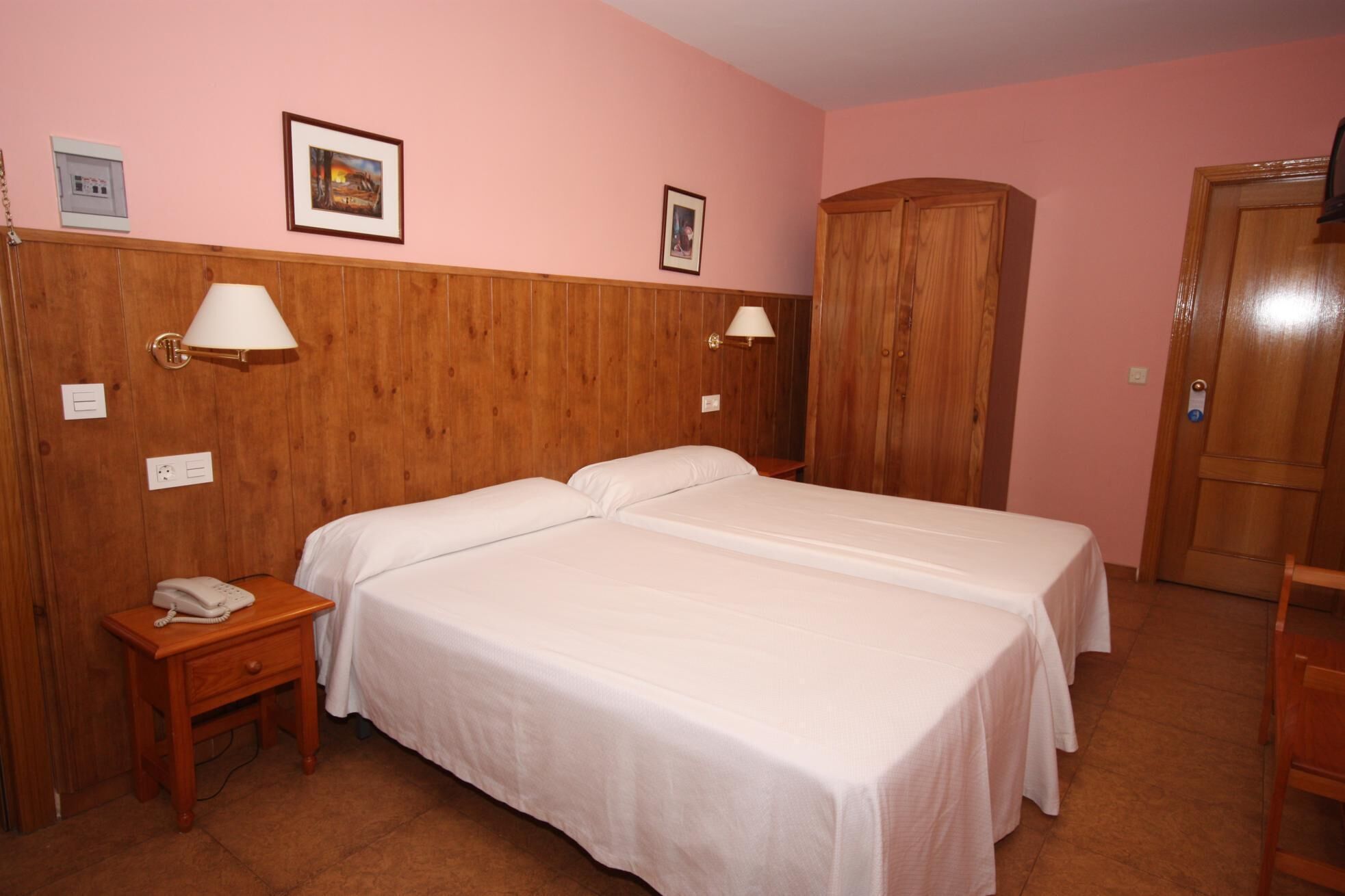 A room with two beds, wooden paneling on the walls, a wardrobe, and a telephone on a nightstand.