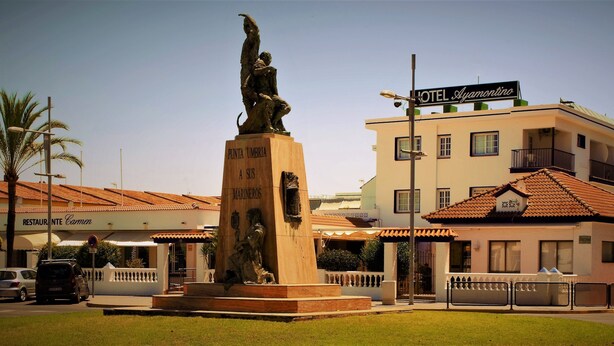 Ett hotell som heter ”HOTEL Ayamontino” med en staty framför, en restaurang som heter ”RESTAURANTE Carmen” till vänster och en byggnad med ett tak täckt av tegelpannor.