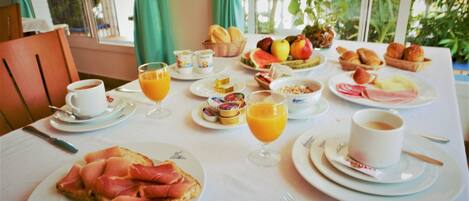 Una mesa de desayuno con diversos alimentos, como pan, fruta y bollería.