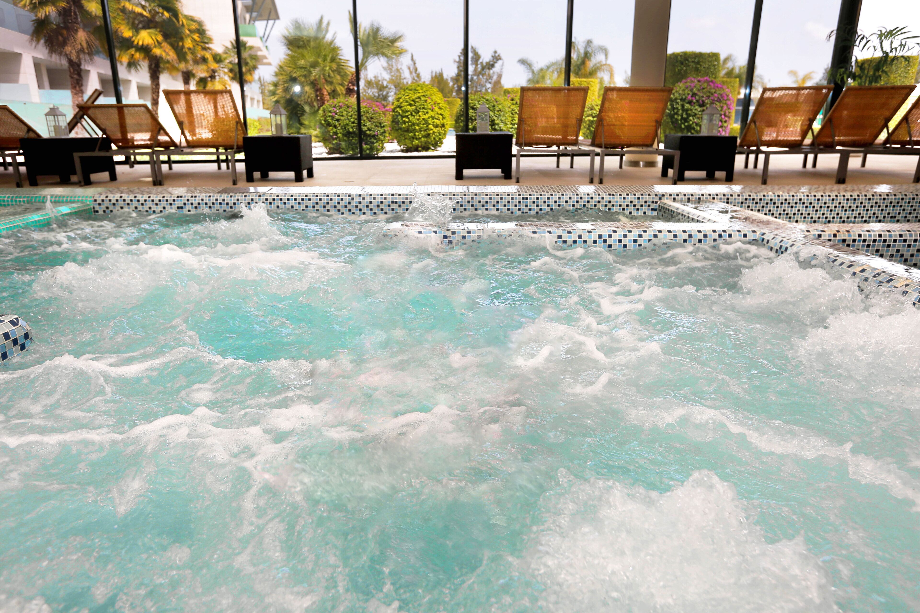 Un jacuzzi con borde de azulejos y una piscina al fondo.
