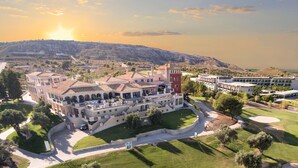 Un gran hotel con varias edificaciones, un campo de golf y montañas al fondo.