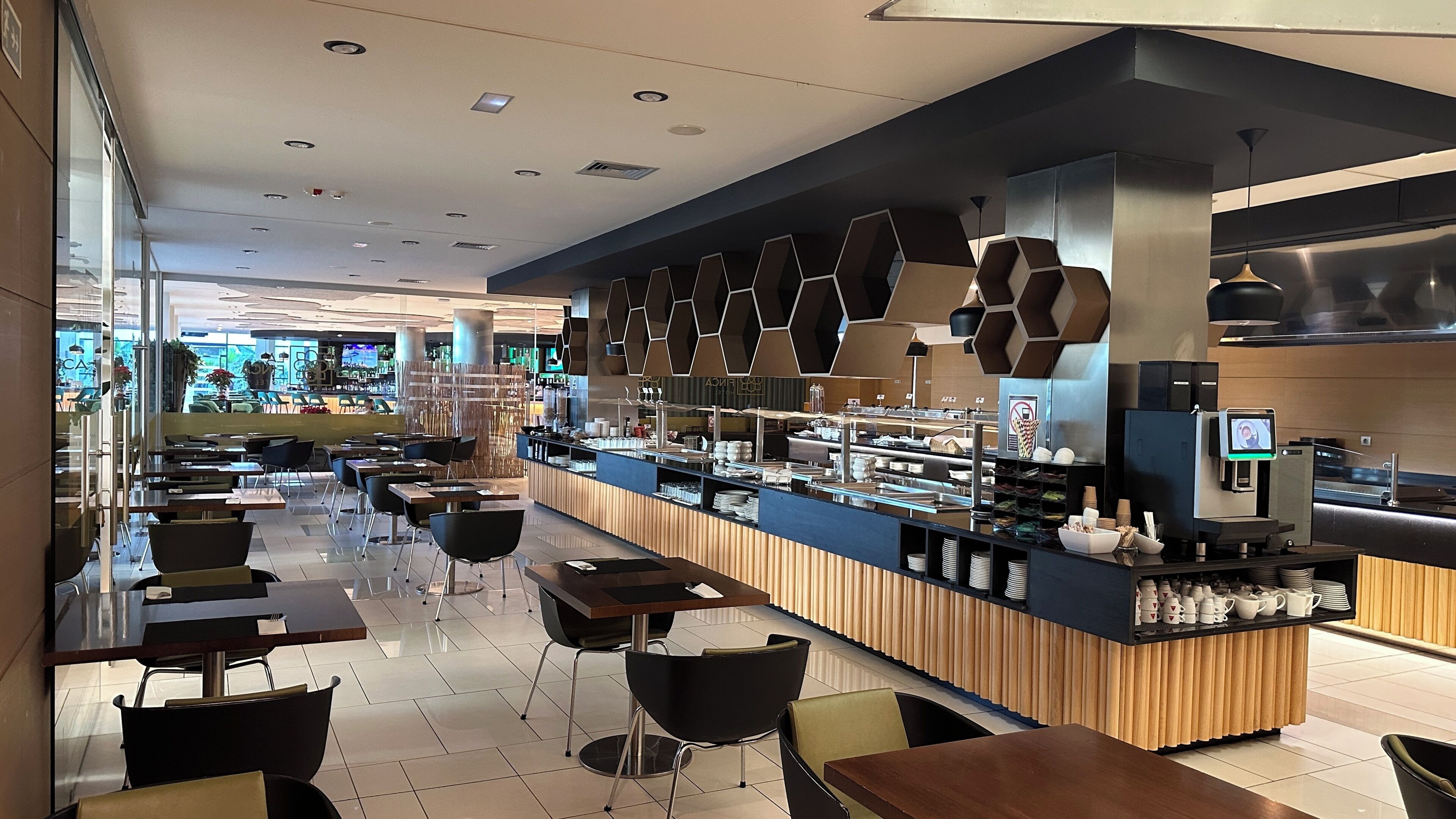 Un café moderno con una barra larga, sillas negras y una amplia variedad de comida y bebidas.