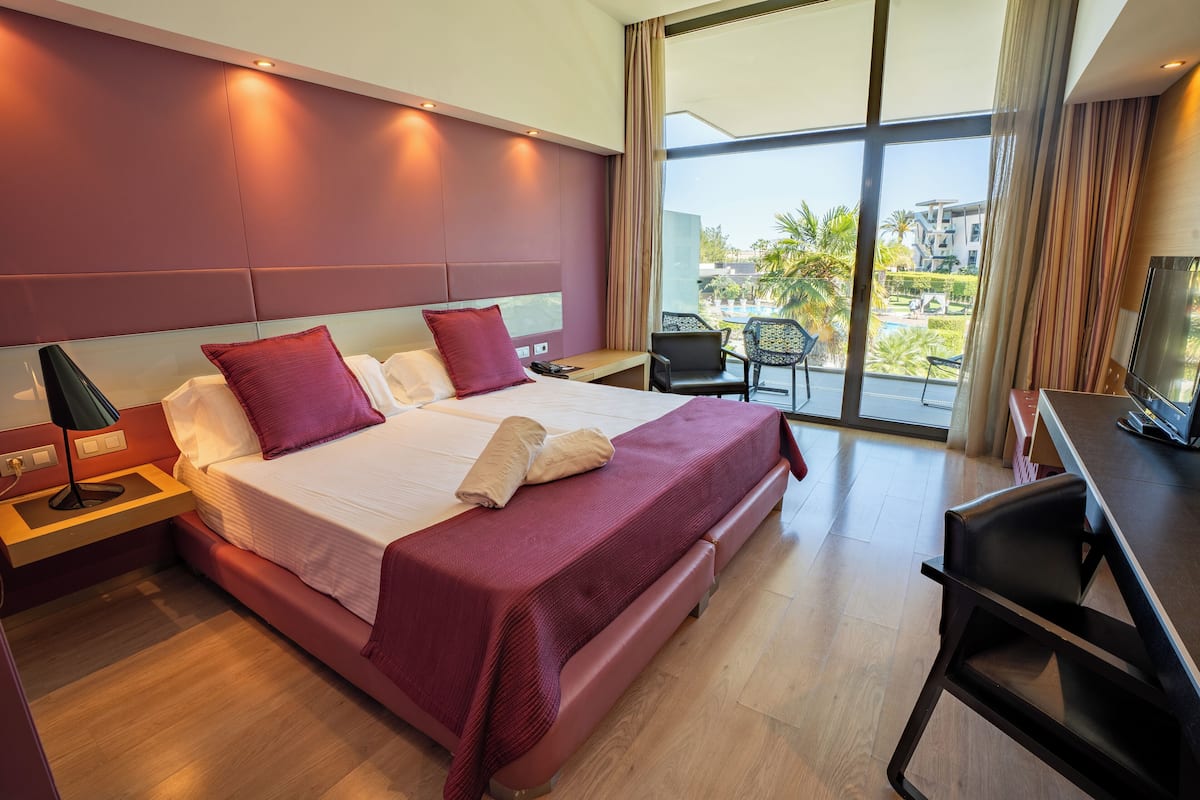 A modern hotel room with a large bed, a desk, and a view of the outdoors.