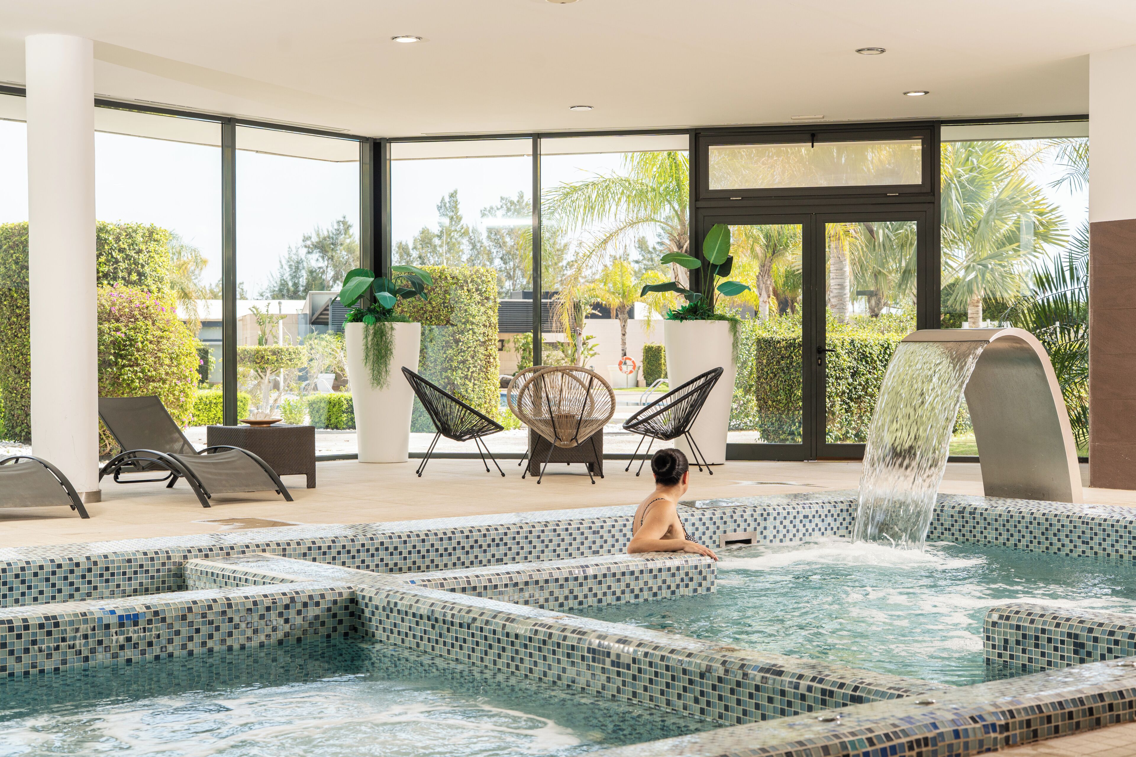 Un espace piscine agrémenté de marches carrelées, de chaises longues et d’une cascade.