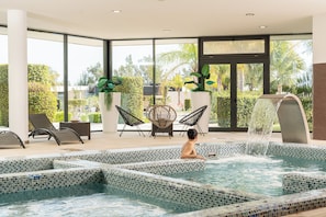A pool area with tiled steps, lounge chairs, and a waterfall feature. - La Finca Resort (Algorfa)